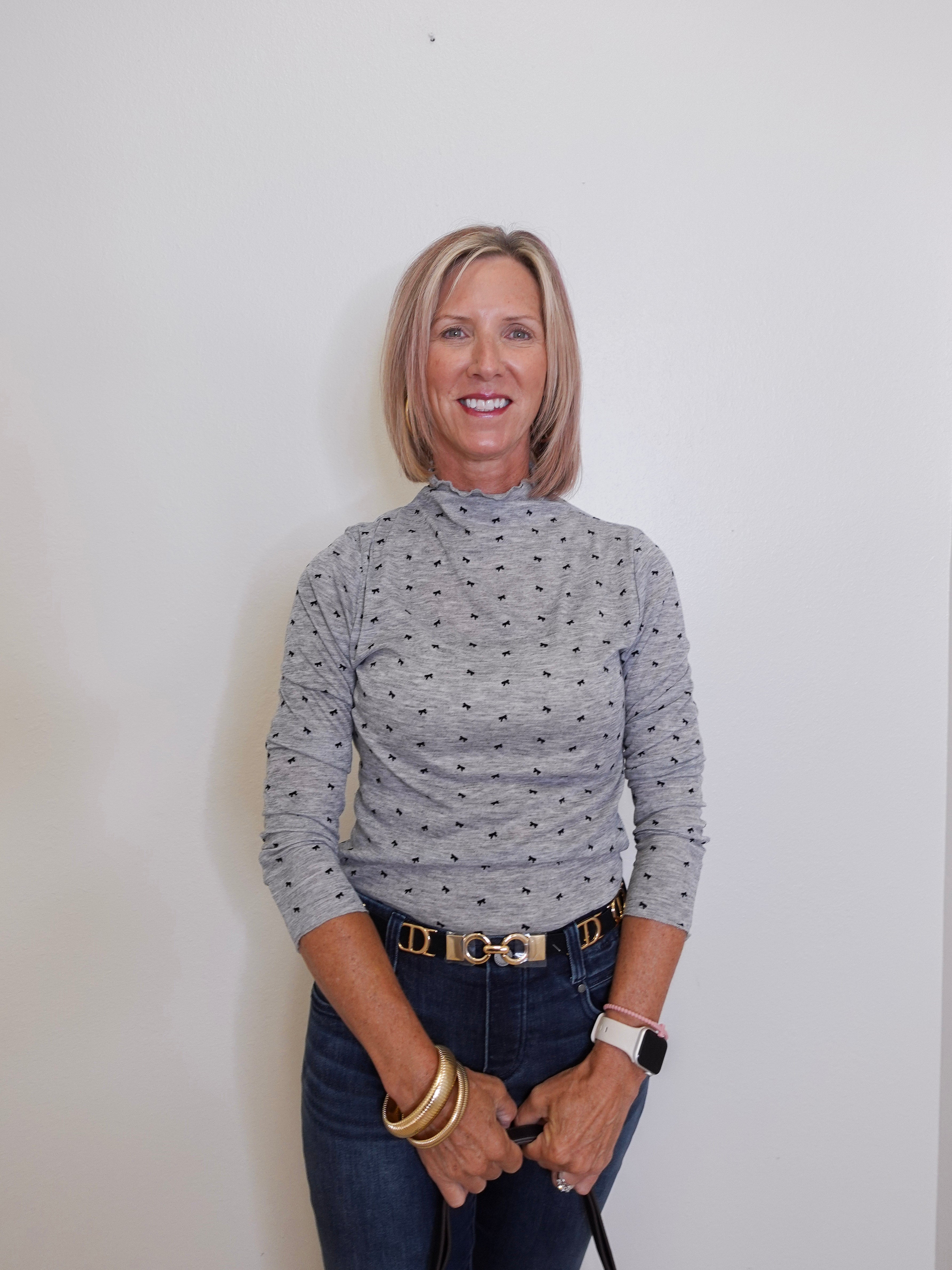 Woman wearing a patterned long-sleeve top and jeans against a plain background