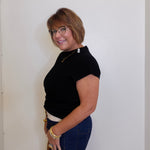 Woman wearing a black top and blue pants against a white wall