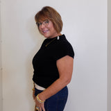 Woman wearing a black top and blue pants against a white wall