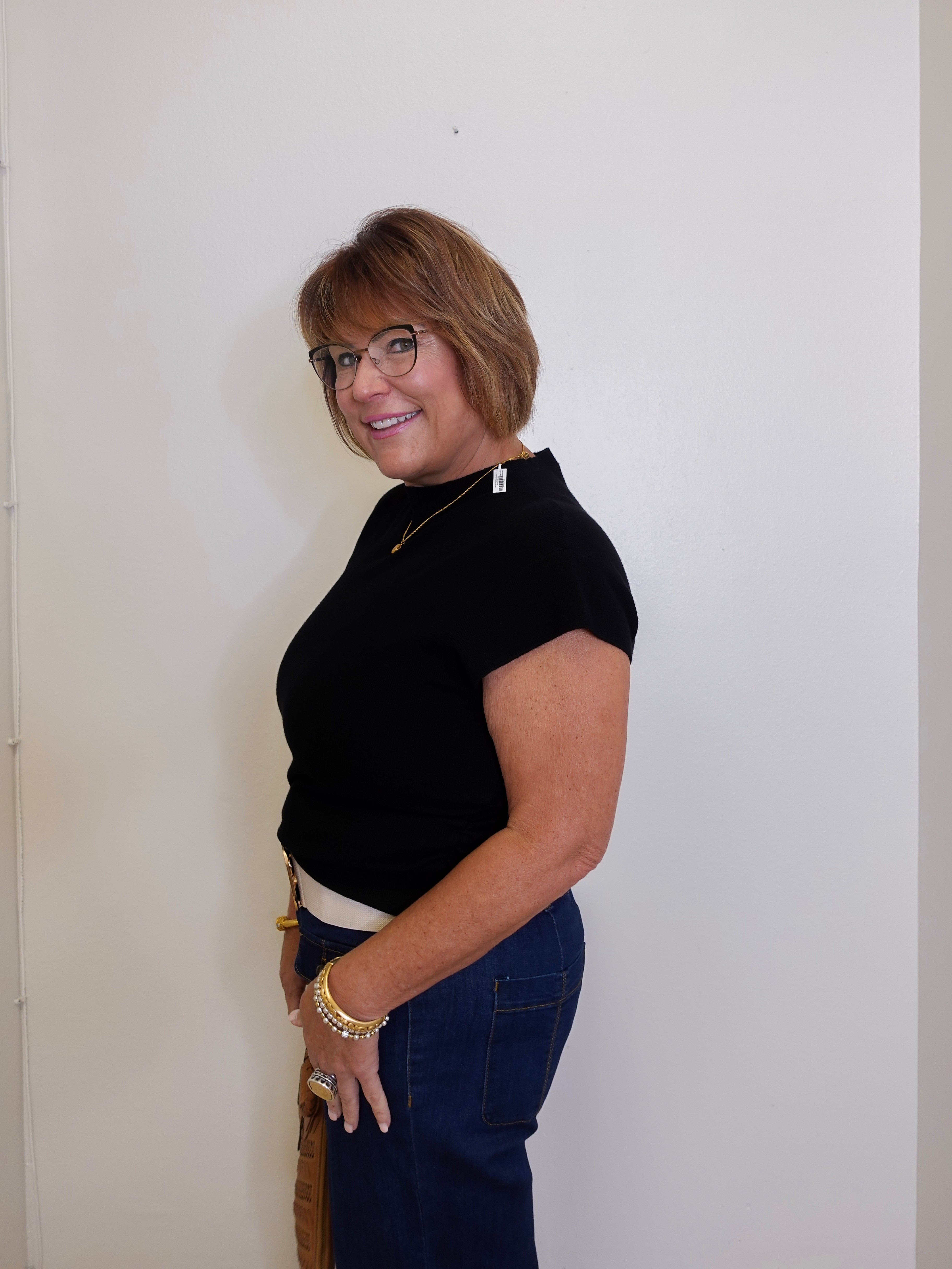 Woman wearing a black top and blue pants against a white wall