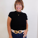 Woman wearing a black top and blue jeans with a gold belt against a white background