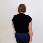 Person wearing a black top and blue jeans against a white wall