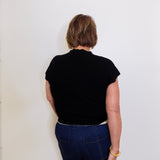 Person wearing a black top and blue jeans against a white wall