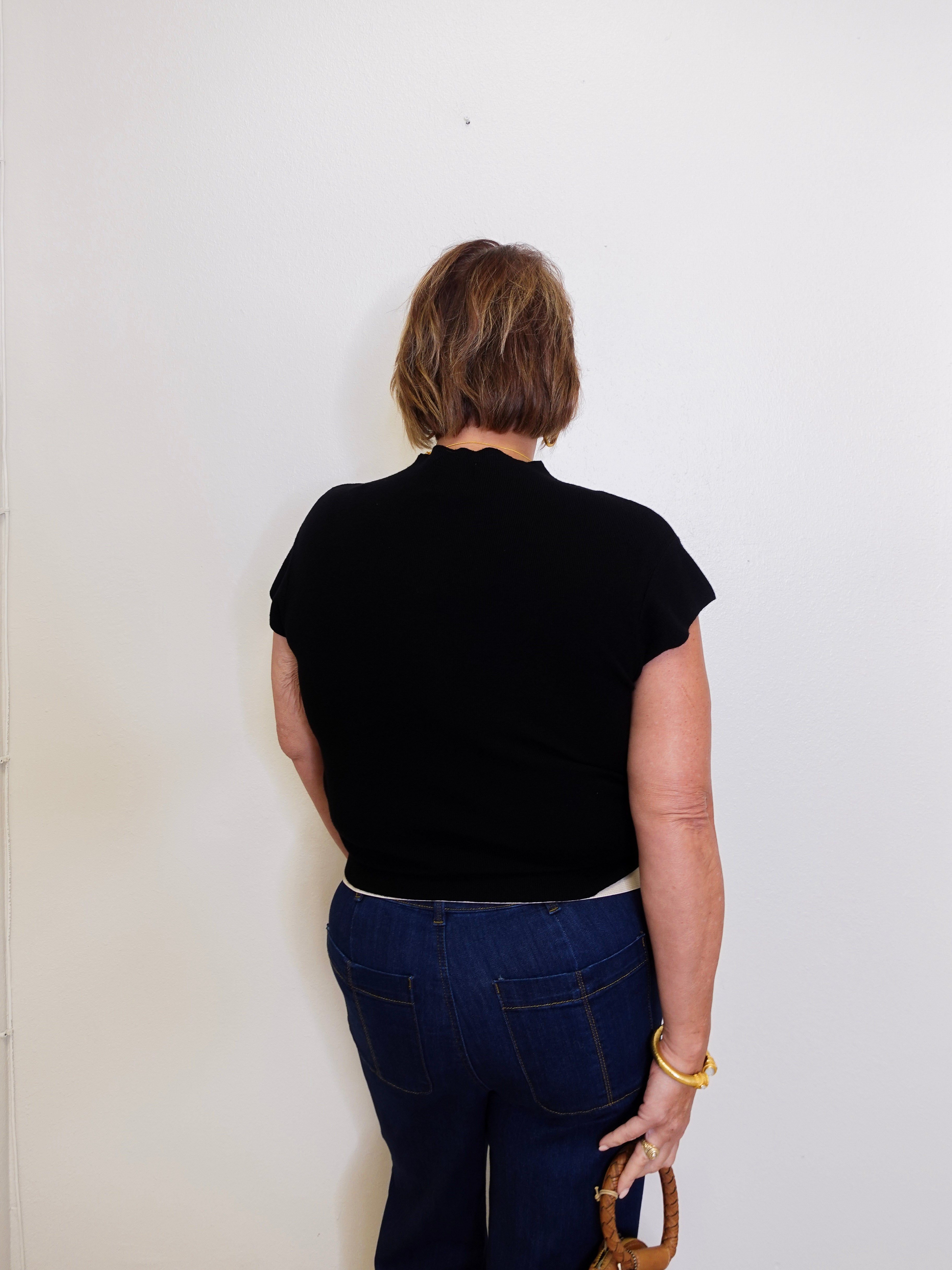 Person wearing a black top and blue jeans against a white wall