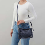 Person wearing a white long-sleeve shirt and blue jeans with a navy blue shoulder bag on a gray background