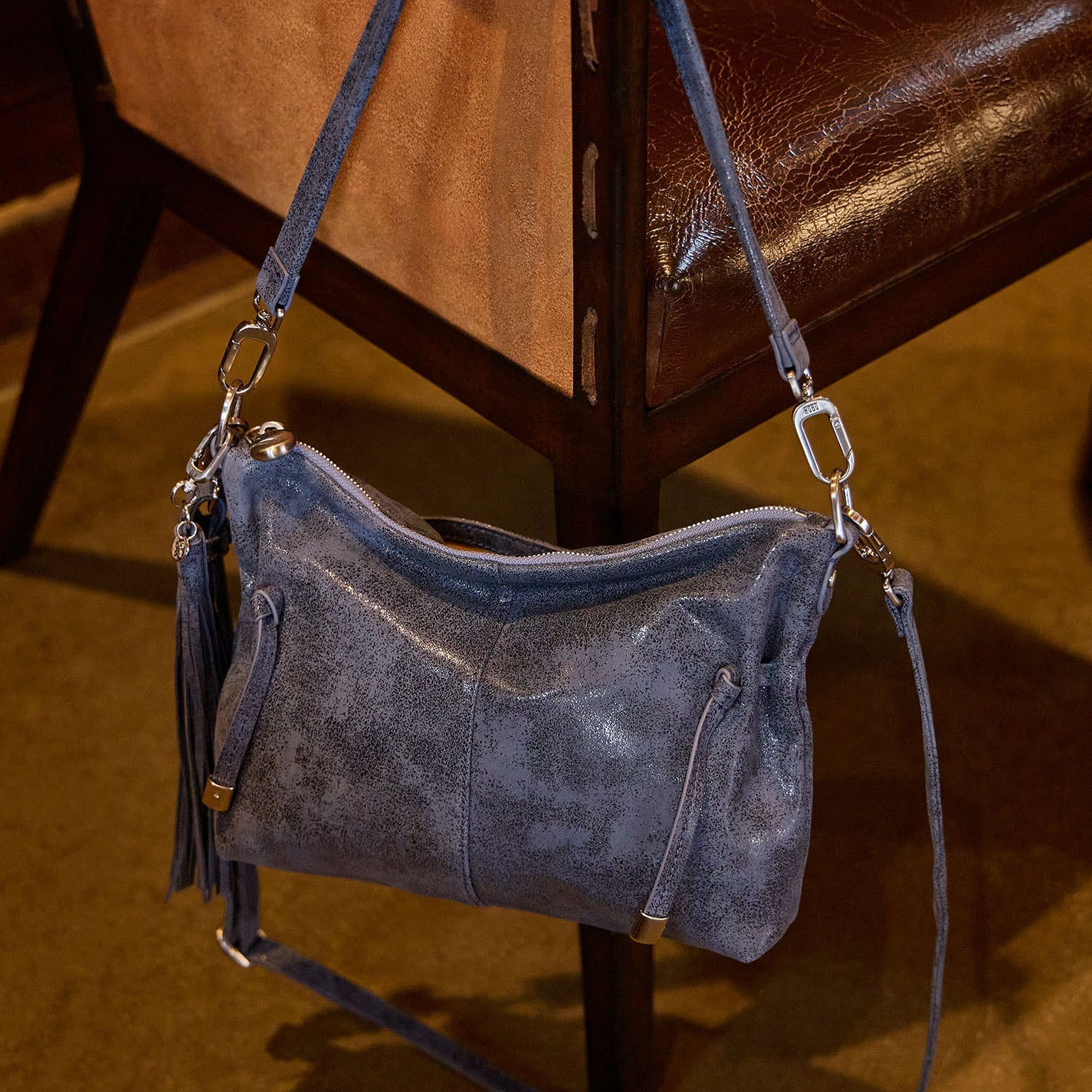 Blue suede handbag with a strap on a brown leather chair.