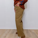 Person wearing a brown sweater, beige pants, and leopard print shoes against a white wall.