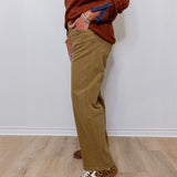 Person wearing a brown sweater, beige pants, and leopard print shoes against a white wall.