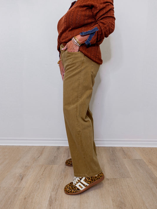 Person wearing a brown sweater, beige pants, and leopard print shoes against a white wall.