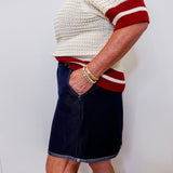 Person wearing a white and red sweater with a navy skirt against a plain background