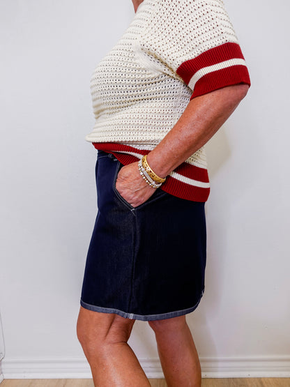 Person wearing a white and red sweater with a navy skirt against a plain background