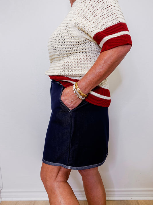 Person wearing a white and red sweater with a navy skirt against a plain background