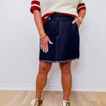 Person wearing a white knit sweater with red accents, navy skirt, and leopard print shoes on a plain background