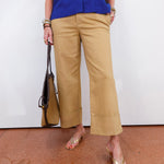 Person wearing a blue shirt and beige pants holding a brown bag on a white background