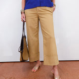 Person wearing a blue shirt and beige pants holding a brown bag on a white background