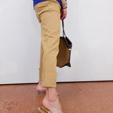 Person wearing beige pants and gold sandals, holding a brown bag on a white background