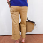 Person wearing a blue top and beige pants, holding a brown bag on a white background
