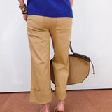 Person wearing a blue top and beige pants, holding a brown bag on a white background