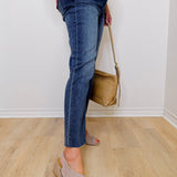 Person wearing blue jeans and beige sandals holding a tan handbag indoors.