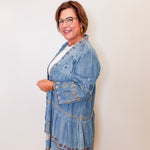 Woman wearing a blue embroidered denim jacket against a white wall.