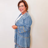 Woman wearing a blue embroidered denim jacket against a white wall.