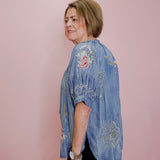 Woman wearing a blue embroidered blouse against a pink wall