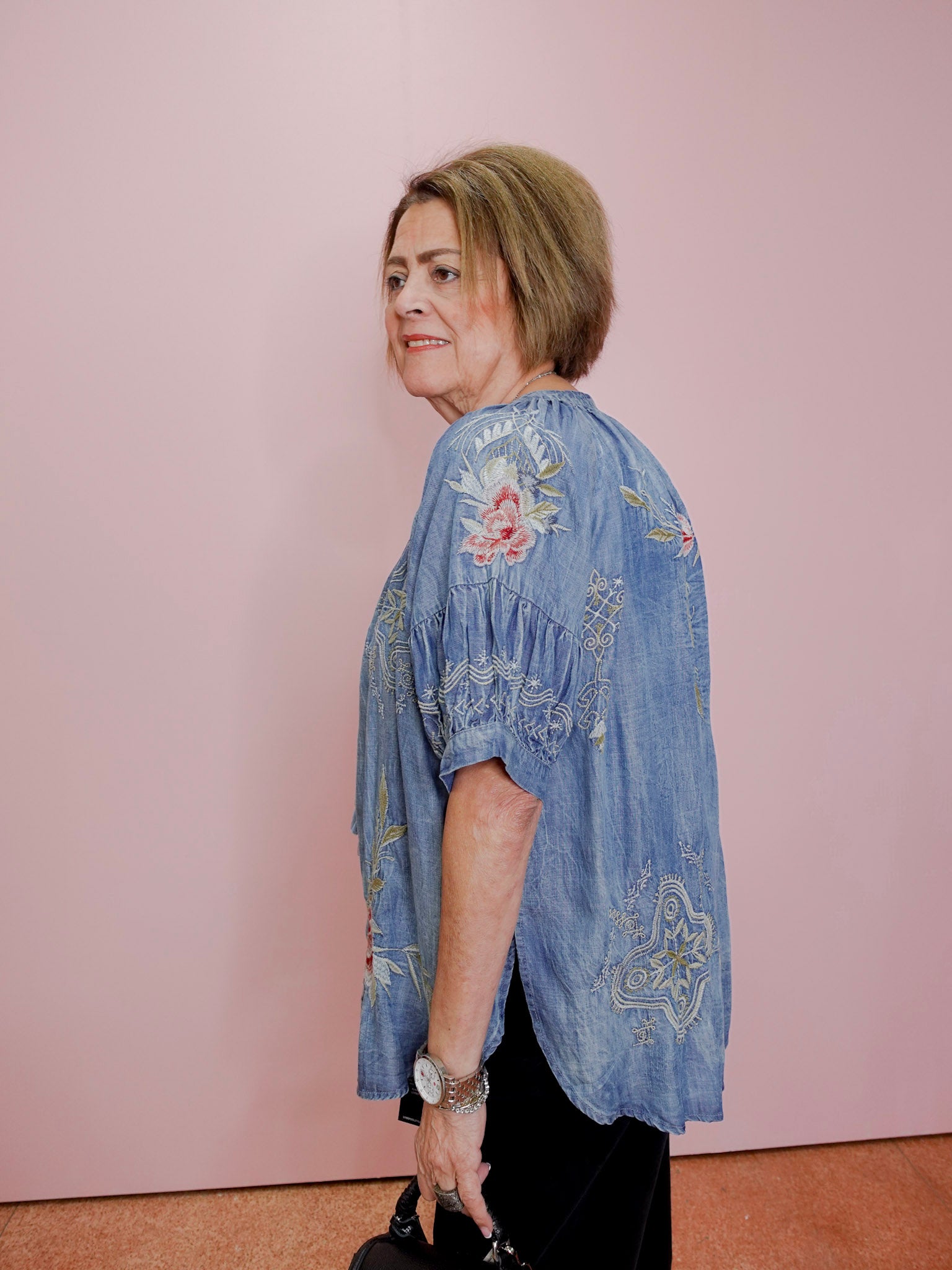 Woman wearing a blue embroidered blouse against a pink wall