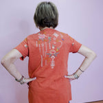 Person wearing an orange t-shirt with a colorful design on the back against a plain background