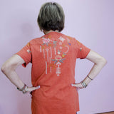 Person wearing an orange t-shirt with a colorful design on the back against a plain background