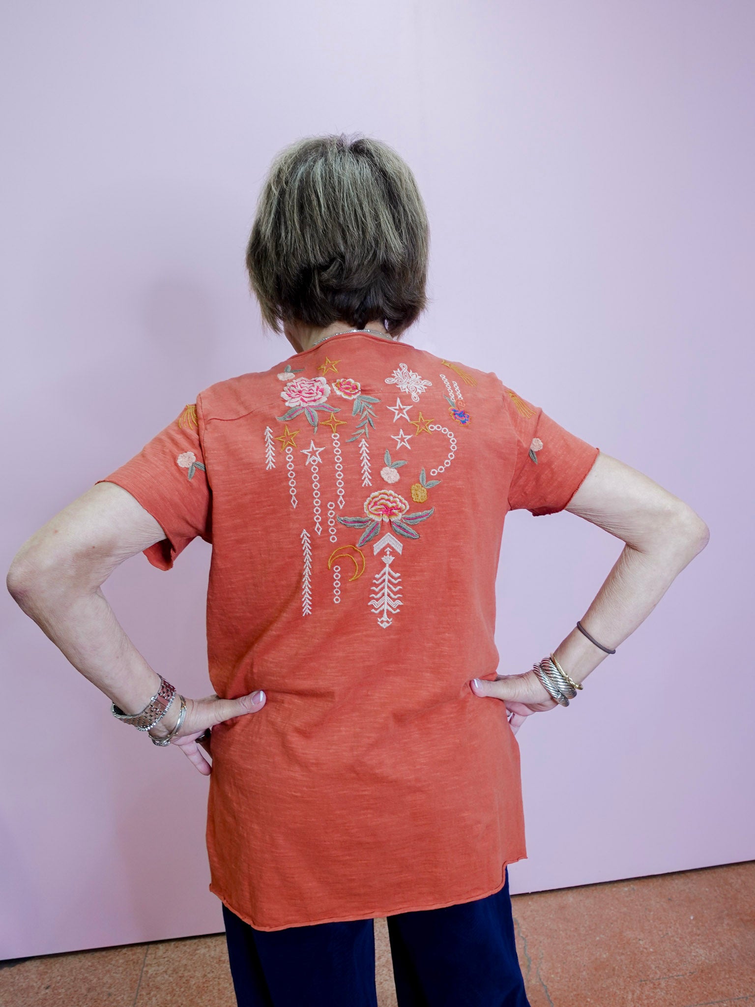 Person wearing an orange t-shirt with a colorful design on the back against a plain background