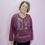 Woman wearing a purple embroidered sweater against a plain background