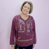 Woman wearing a purple embroidered sweater against a plain background