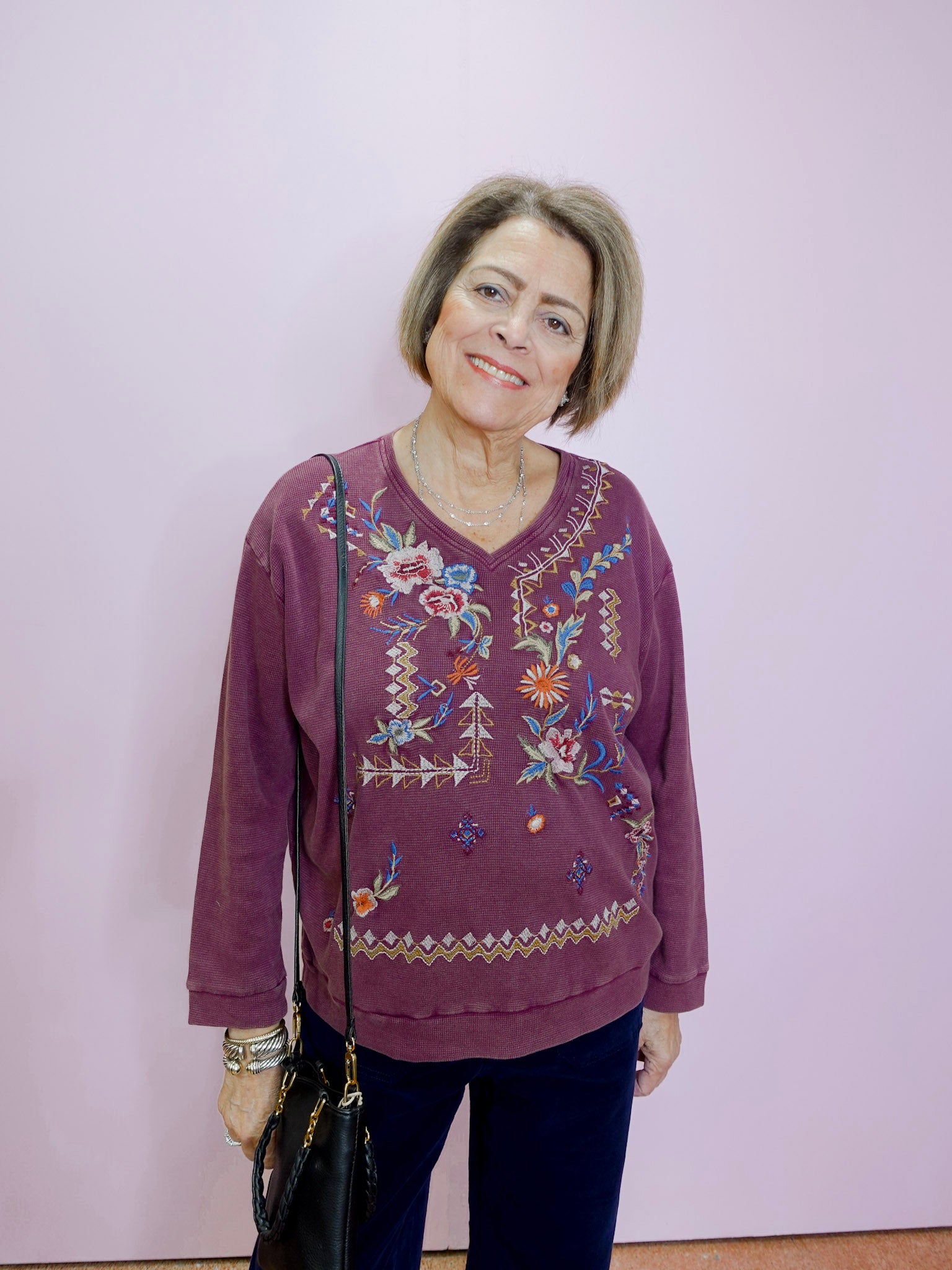 Woman wearing a purple embroidered sweater against a plain background