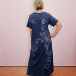 Person wearing a blue dress with floral patterns against a pink wall.