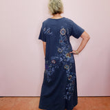 Person wearing a blue dress with floral patterns against a pink wall.