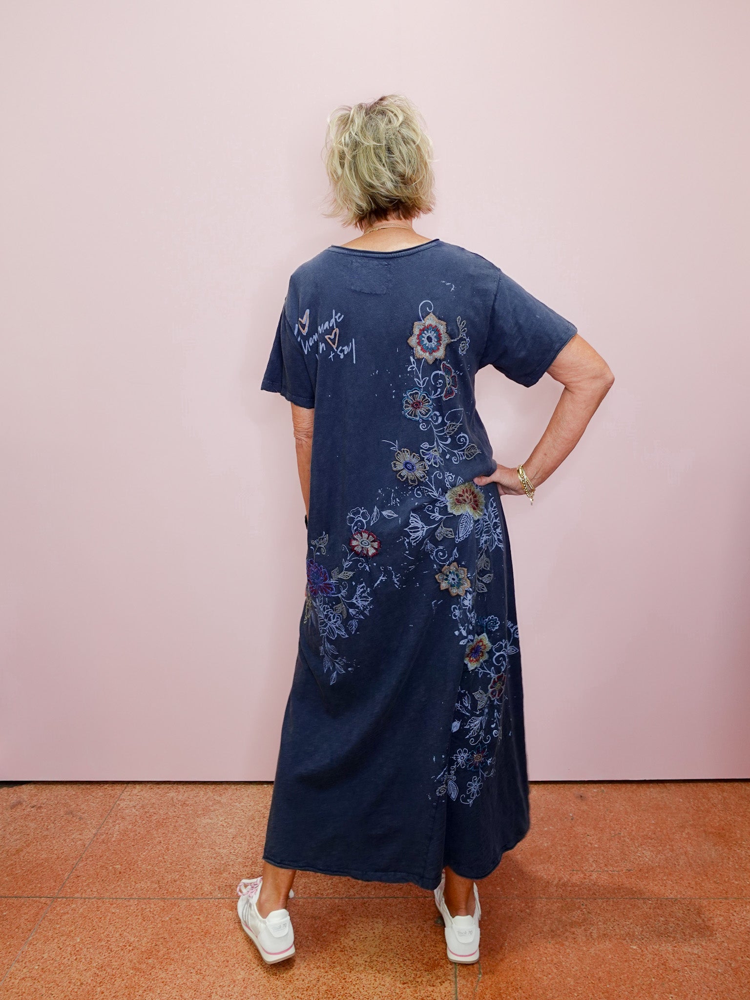 Person wearing a blue dress with floral patterns against a pink wall.