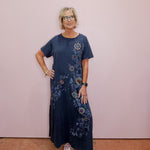 Woman wearing a blue floral dress standing against a pink wall.