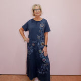 Woman wearing a blue floral dress standing against a pink wall.