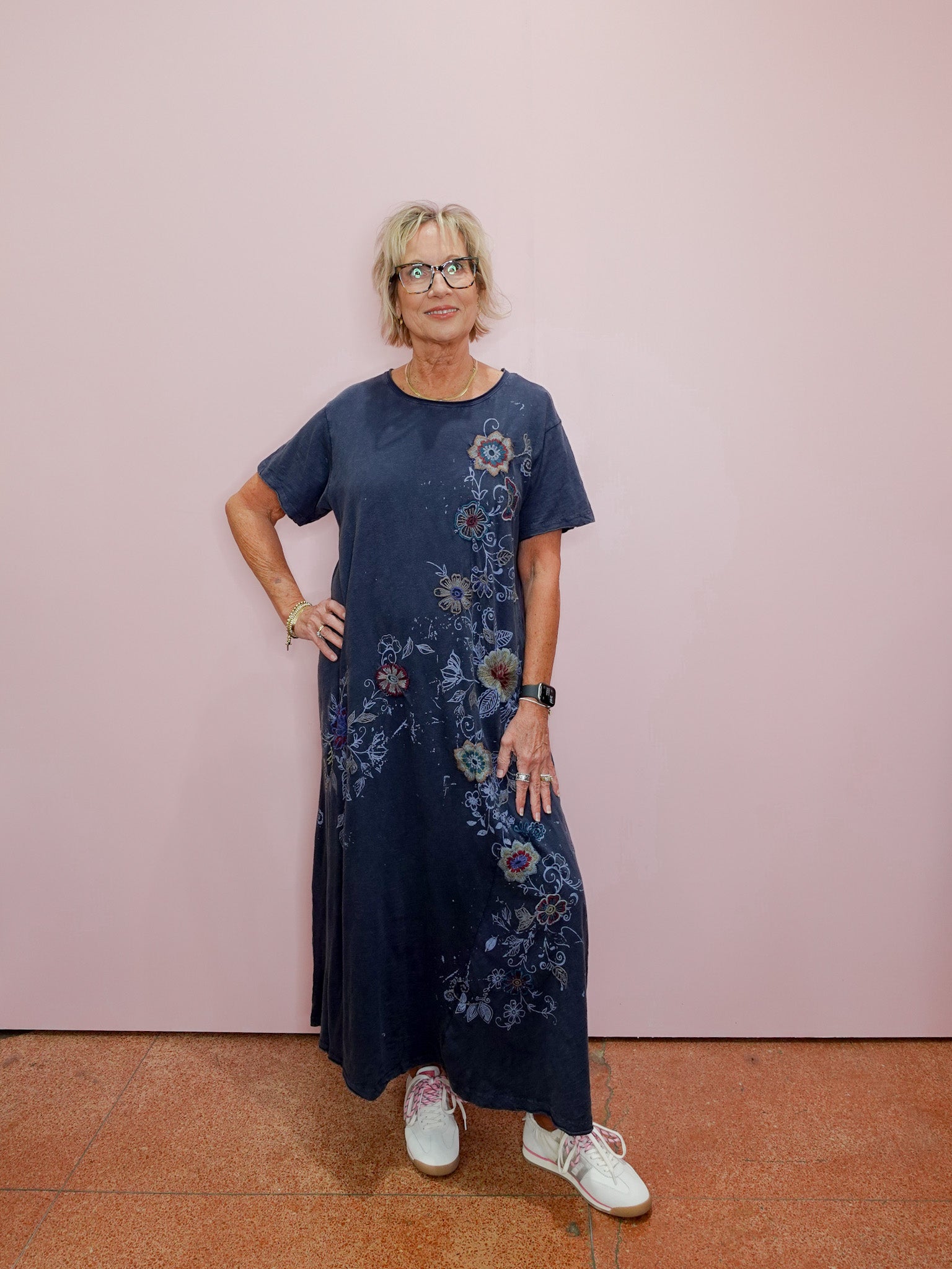 Woman wearing a blue floral dress standing against a pink wall.