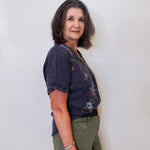 Woman wearing a dark blue floral blouse and green pants against a white background