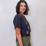 Woman wearing a dark blue floral blouse and green pants against a white background