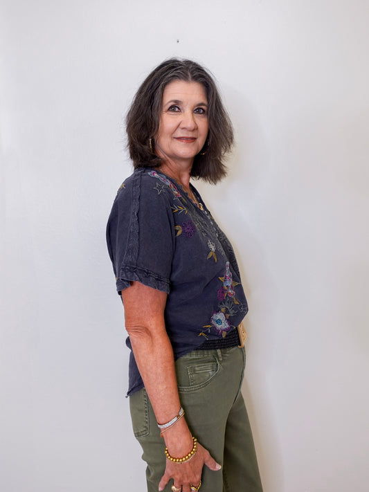 Woman wearing a dark blue floral blouse and green pants against a white background