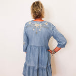 Woman wearing a blue denim dress with floral embroidery on a white background