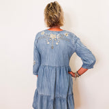 Woman wearing a blue denim dress with floral embroidery on a white background