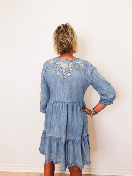 Woman wearing a blue denim dress with floral embroidery on a white background