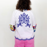 Person wearing a white shirt with blue floral design and colorful sleeves, paired with pink shorts on a white background.