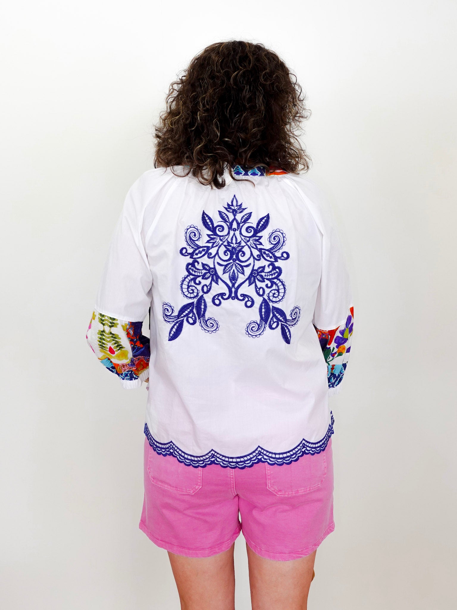 Person wearing a white shirt with blue floral design and colorful sleeves, paired with pink shorts on a white background.