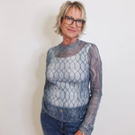 Woman wearing a sheer fishnet top and jeans against a plain background