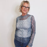 Woman wearing a sheer fishnet top and jeans against a plain background