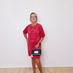Woman in a red dress holding a small bag against a white wall